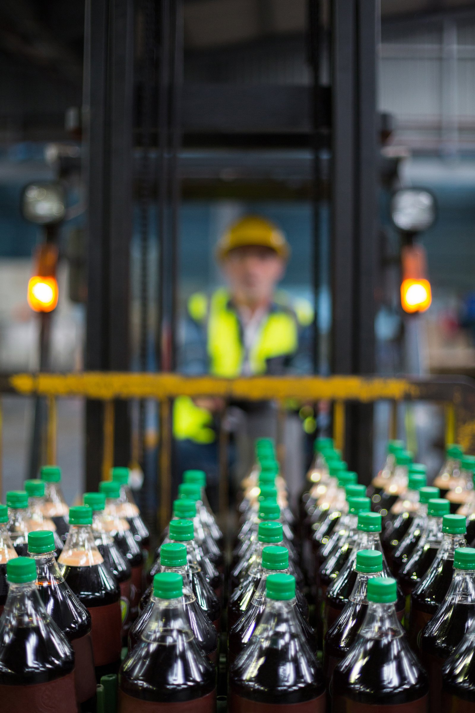 Capped soft-drink bottles on a line with a forklift operator behind