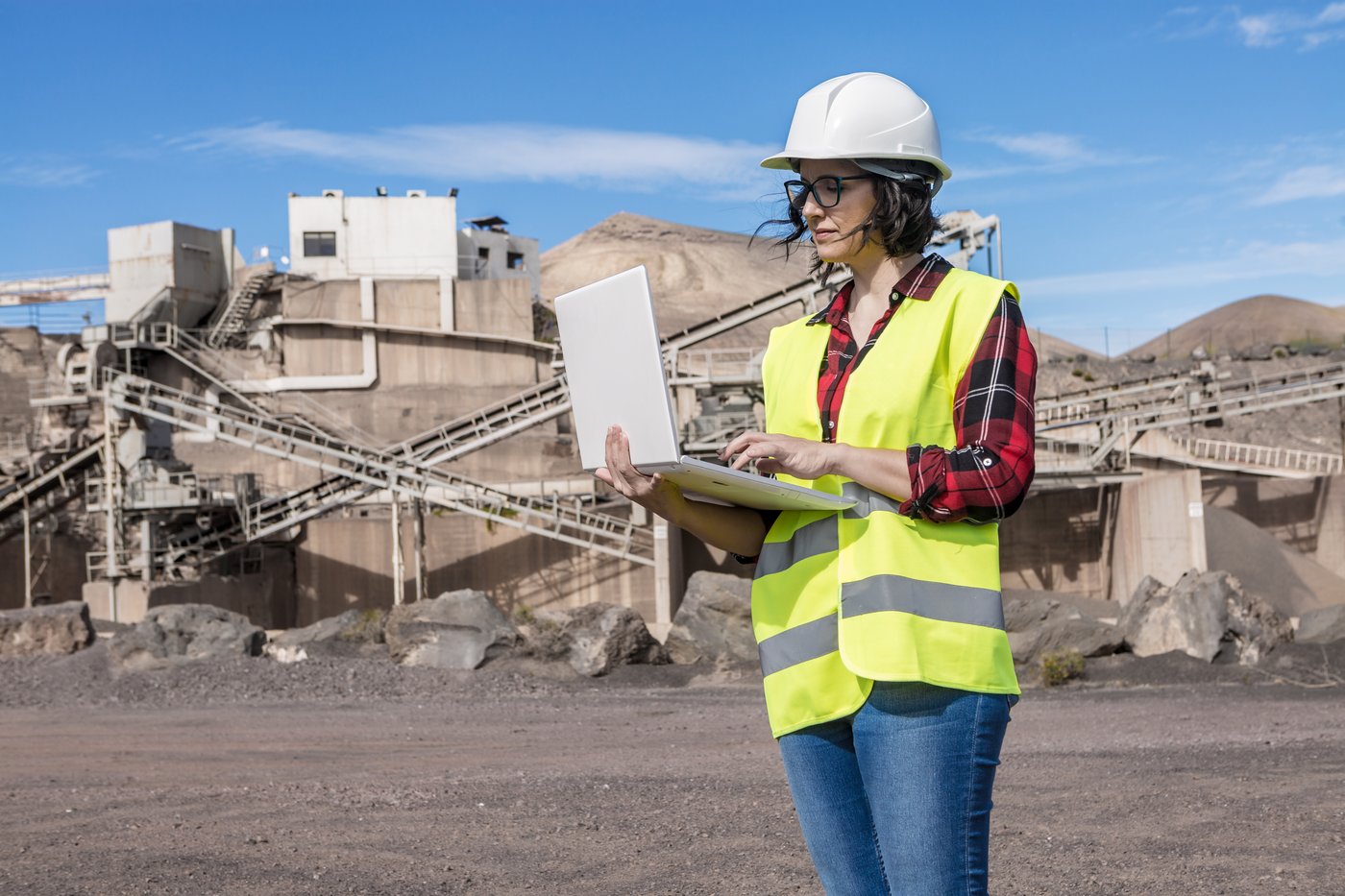 Engineer in a hard hat reviewing data on a laptop at a quarry