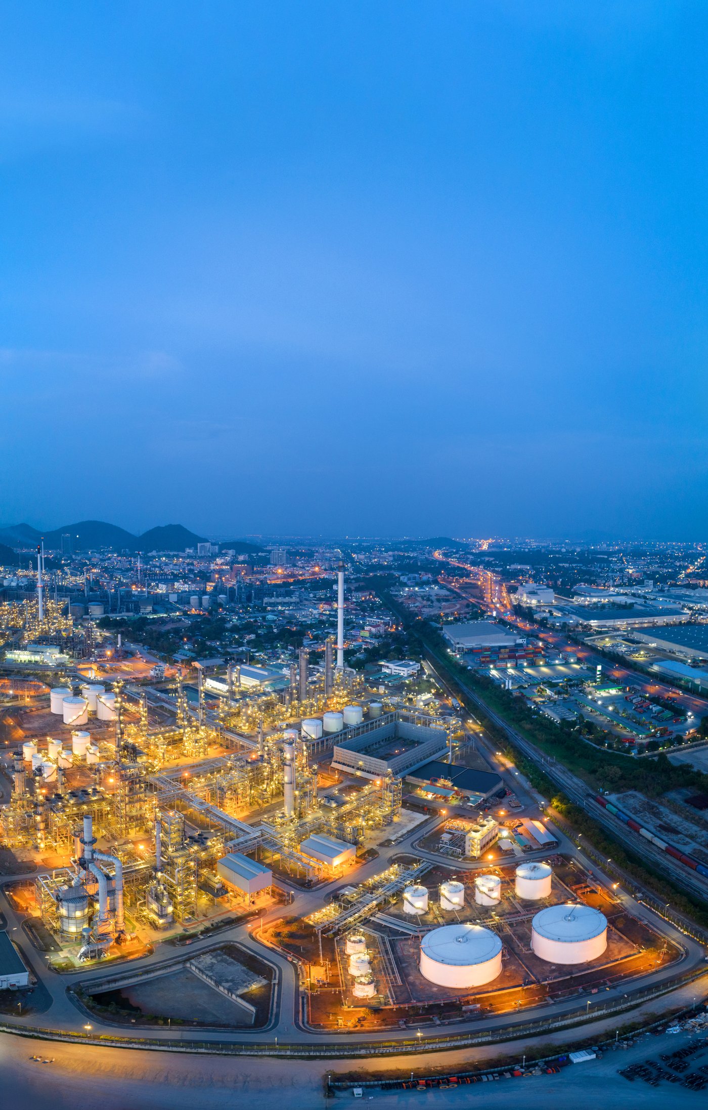 Refinery complex lit at dusk under a blue sky