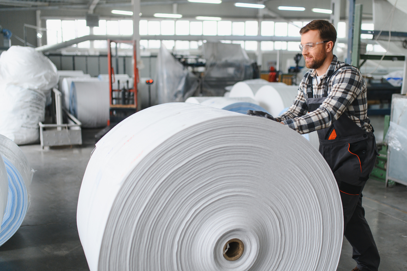 Worker pushing a large white paper roll in a mill
