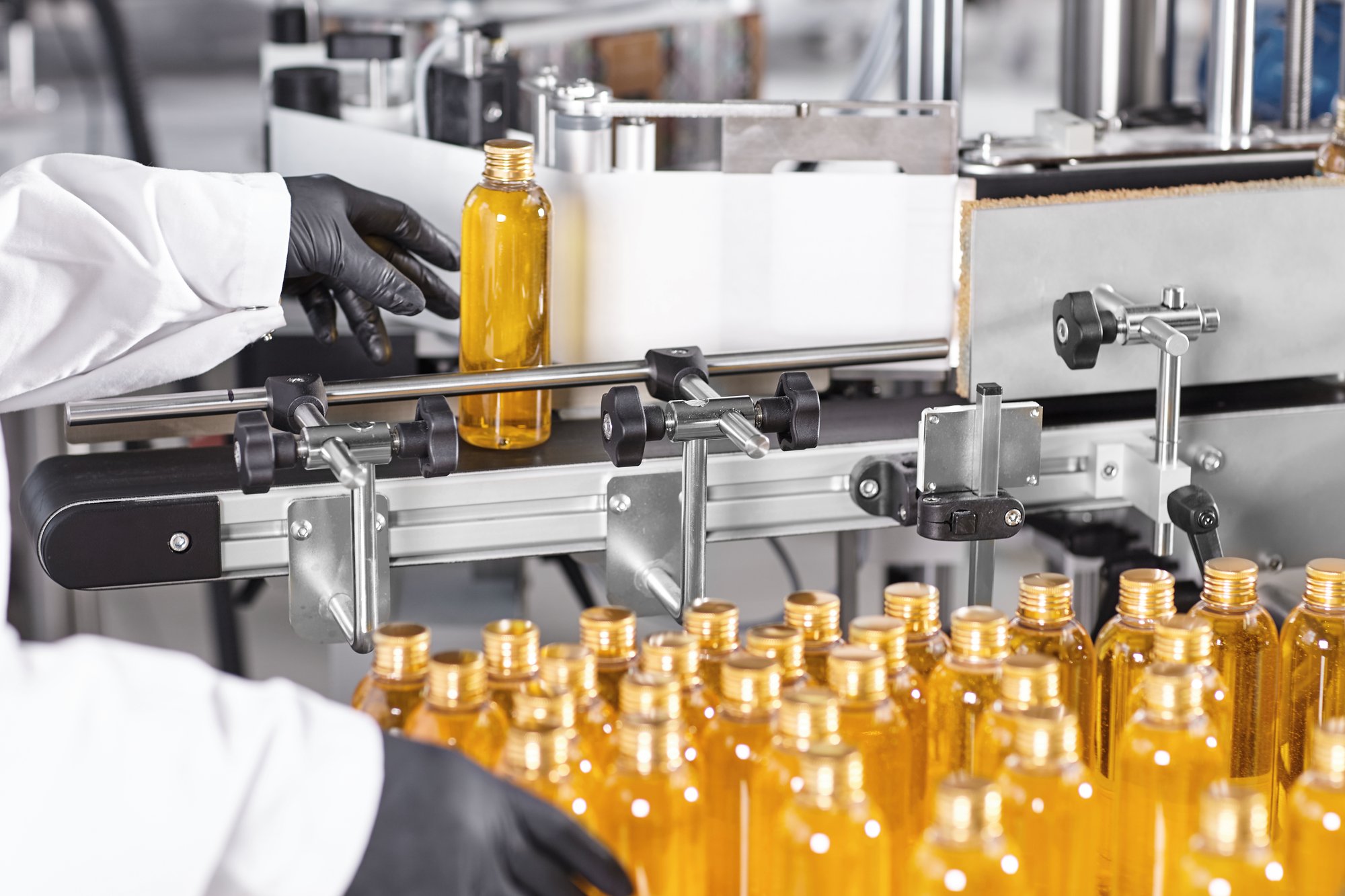 Gloved operator guiding bottles through a labelling line