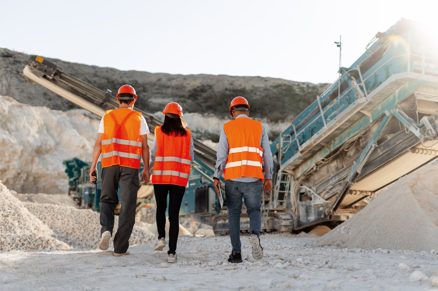 Three workers in hard hats walking toward a mobile crusher